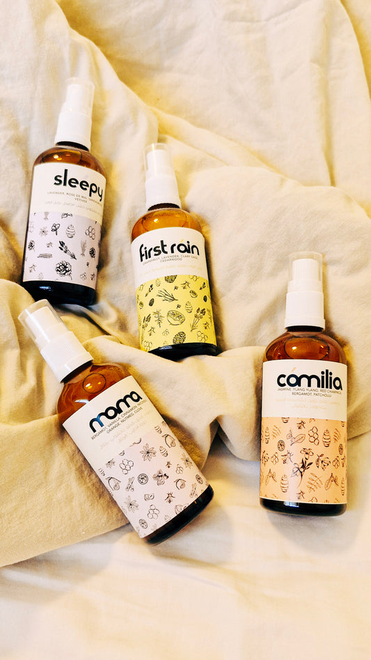Four bottles labeled 'sleepy', 'first rain', 'noma', and 'camilla' on a textured beige surface.