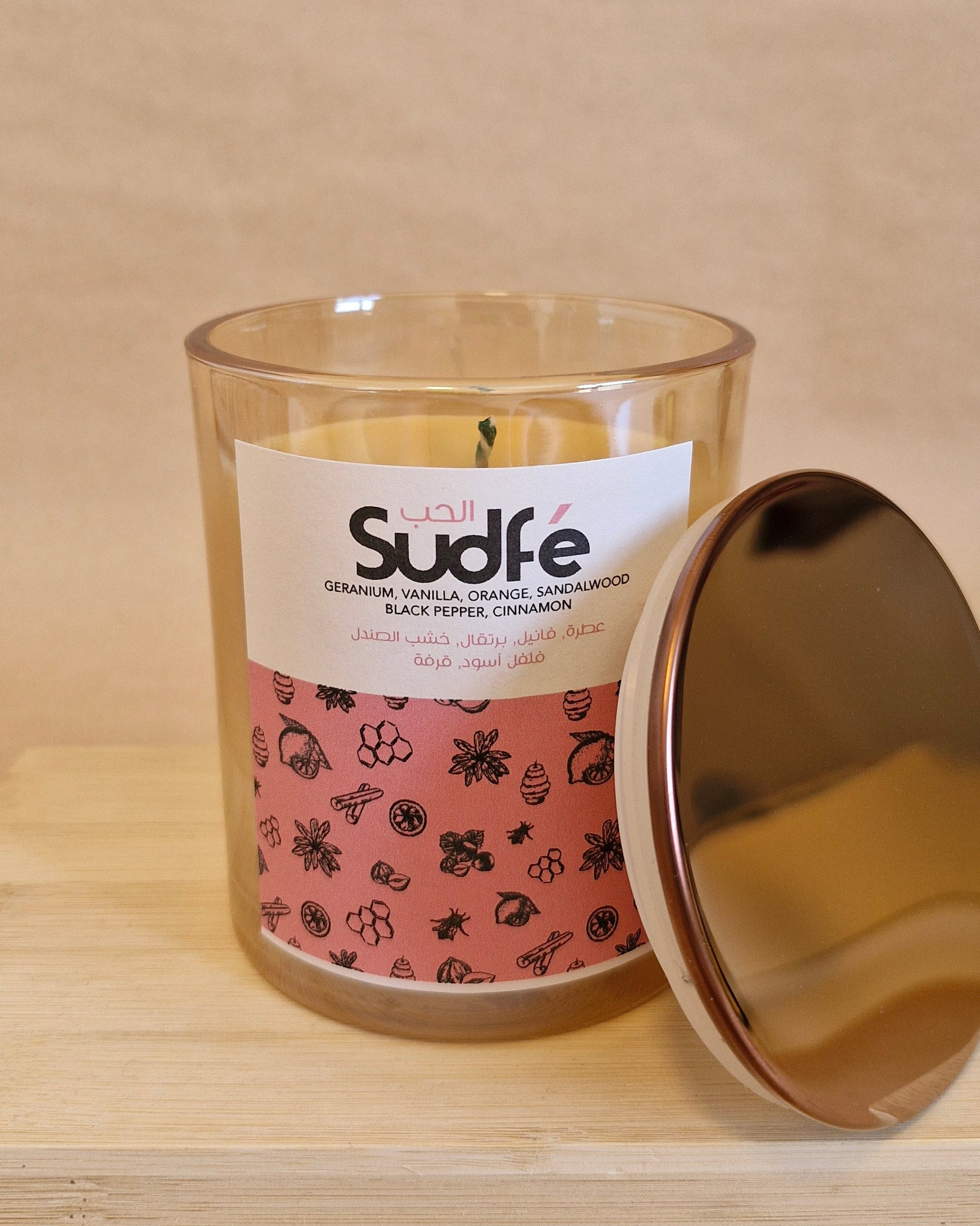 Glass candle with a gold lid on a beige surface, featuring a 'Sudafe' label.